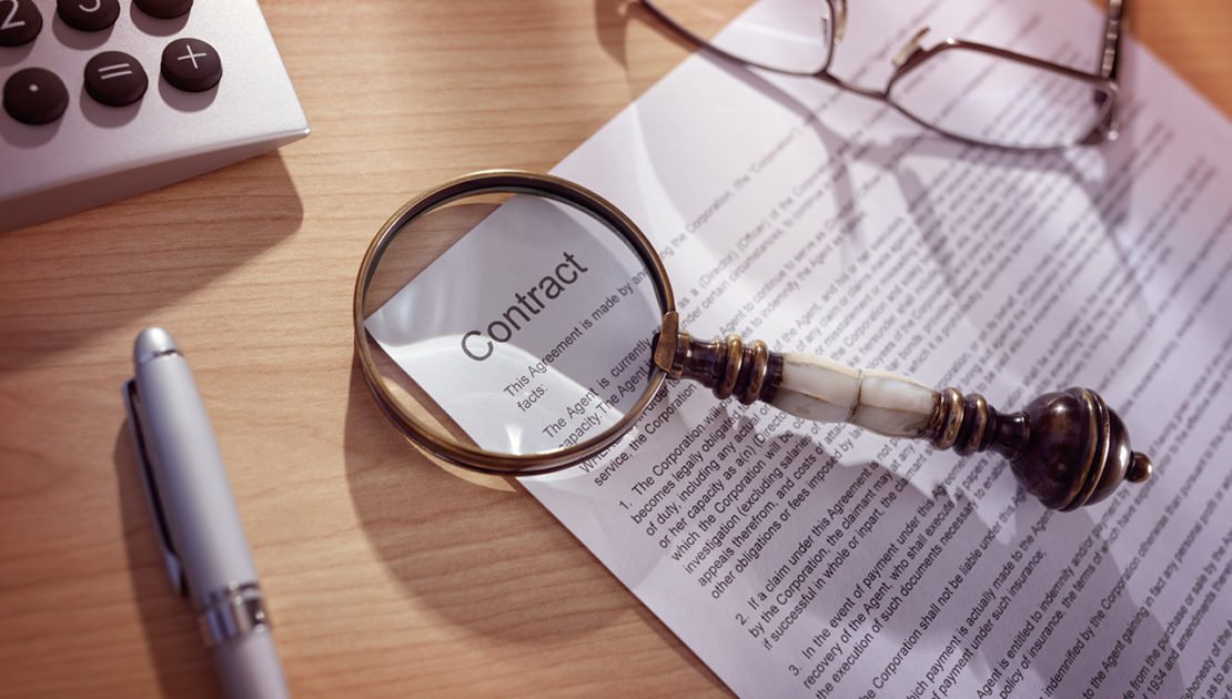 Magnifying glass examining and signing a legal contract document